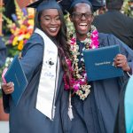 Two happy graduates smiling with their degrees.