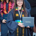 Smiling graduate holding degree and wearing Puente stole.