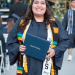 Smiling graduate holding degree and wearing Puente and EOPS stole.