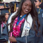 Smiling graduate wearing EOPS stole and pink lei.