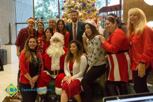 Staff dressed in red surrounding Santa Claus.