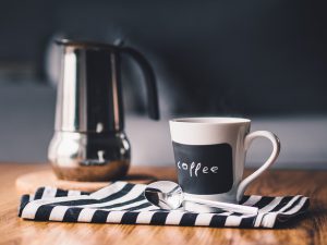 Coffee pot, mug, and black and white striped dish towel sitting on a wooden table