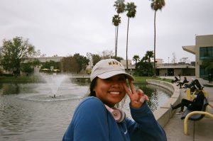 Student smiling and giving peace sign with pond behind her.