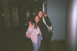 Two young ladies, smiling and giving the peace sign.