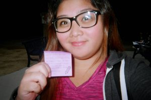Young woman with glasses, holding up a post it note.