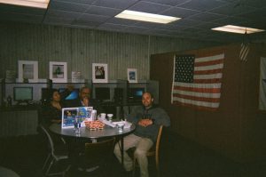 People sitting at a round table smiling with the American flag in the background.