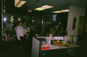 Students standing around a desk smiling.