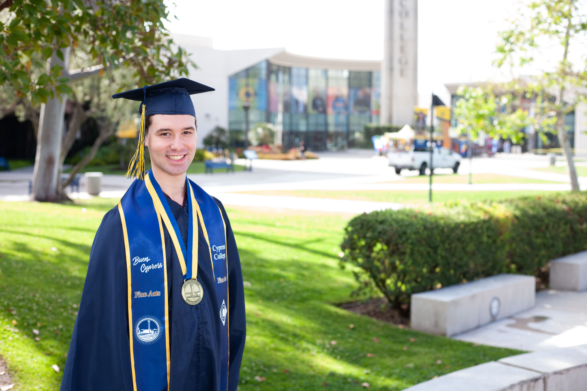 Portrait of Preston Harris, the 2023 Presidential Scholar of Distinction for the Fine Arts pathway, wearing regalia with Gateway Plaza, including the Student Center and Campanile, in the background.