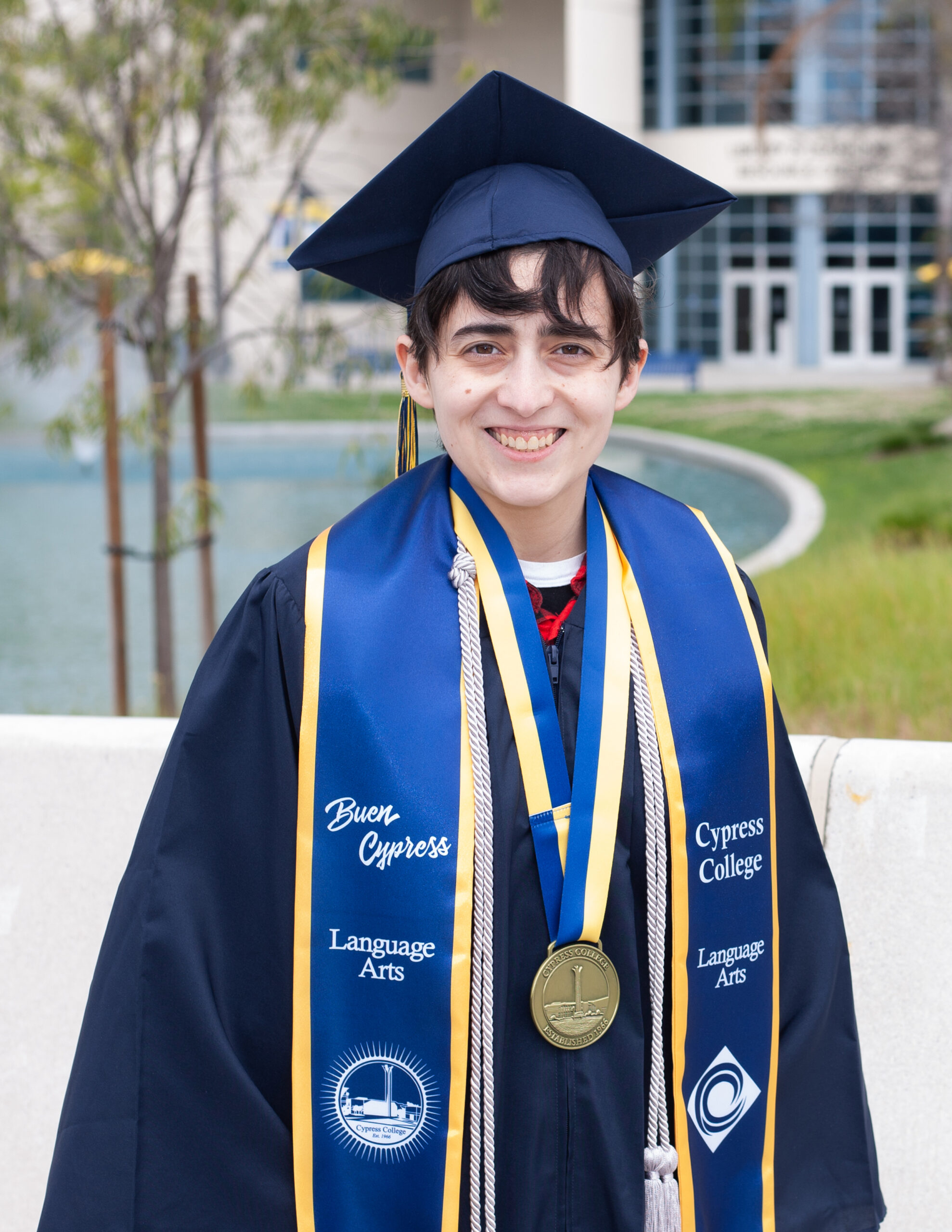 Portrait of Olly Tetrault, the 2023 Presidential Scholar of Distinction for the Language Arts pathway, wearing regalia with the pond in the background.