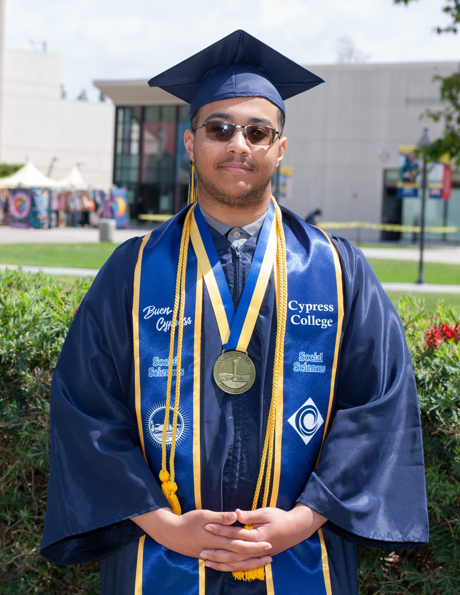 Portrait of Selwyn Gibson, the 2023 Presidential Scholar of Distinction for the Social Sciences pathway, wearing regalia with Gateway Plaza and Bookstore in the background.