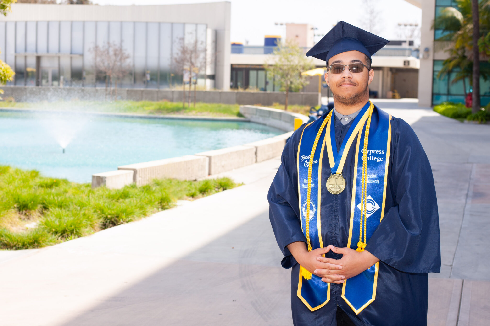 Portrait of Selwyn Gibson, the 2023 Presidential Scholar of Distinction for the Social Sciences pathway, wearing regalia with the pond in the background.