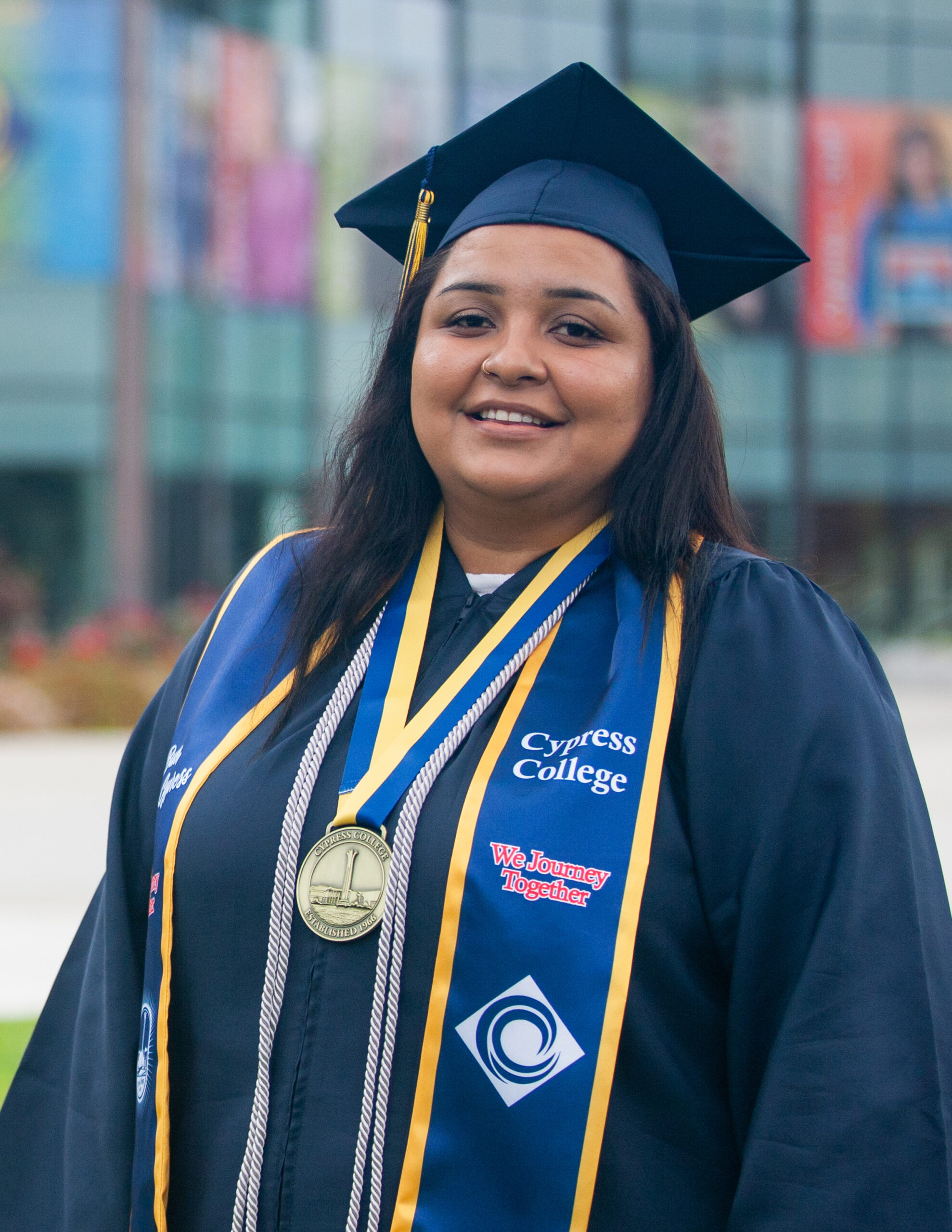Portrait of Azusena Zamarripa, the 2023 Presidential Scholar of Distinction for the We Journey Together pathway, wearing regalia with Gateway Plaza and Student Center in the background.