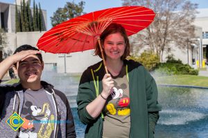 Male and female students wearing Mickey Mouse shirts and holding a red umbrella