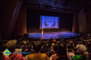 Audience watching woman on stage with cartoon on big screen.