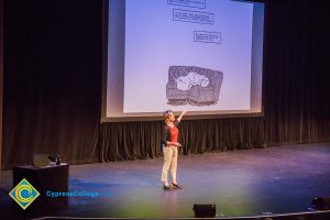 Woman standing on stage pointing to a big screen.