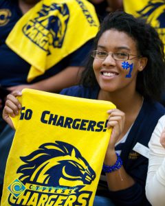 A female fan with glasses and #1 painted on her face in blue, holds up a yellow Chargers towel.