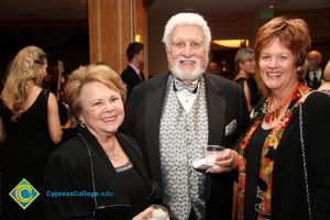 Man with grey hair and beard holding a drink and smiling with two women.