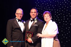 President Bob Simpson with a man in a black suit and tie holding an award with a woman in a tan dress and white shoulder wrap.