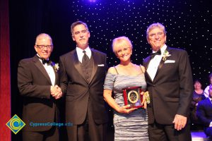 President Bob Simpson with two men in a black suits and tie and a woman in a grey dress holding an award.