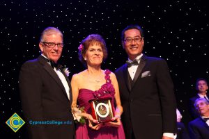 President Bob Simpson with a man in a black suit and tie and a woman in a fuchsia dress holding an award.