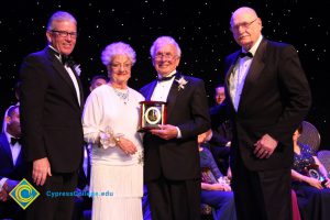 President Bob Simpson and another man in a suit with a couple who are holding an award.