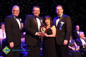 Men in suits and tie with a woman in a black dress holding an award.