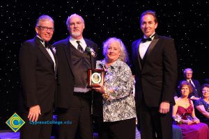 Men in suits, standing around a woman holding an award.