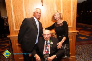 Scott Pickler in a suit and tie with a man in a wheelchair wearing a medal around his neck and a woman standing in a black dress.