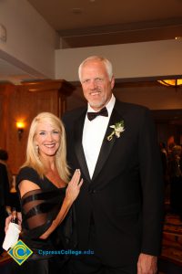 A very tall man in a black suit and bowtie with a blonde woman in a black dress.
