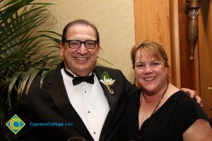 A man in a black suit and bowtie and a woman in black smiling.