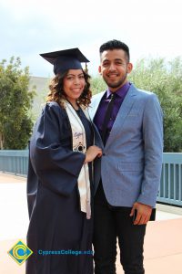 A young man in a light blue suit with shirt and tie and a young lady in her cap and gown.