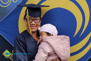 A young lady in her cap and gown holding a sleeping baby.