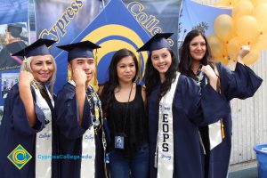 A group of EOPS graduates in cap and gown flexing muscles.