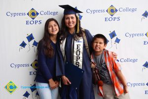 An EOPS graduate in cap and gown with a young girl and a young boy.