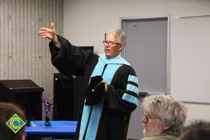 President Bob Simpson in graduation regalia with hand outstretched.