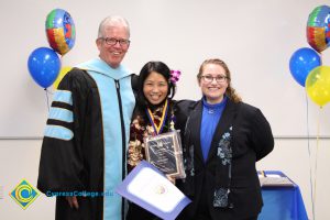 A young woman with a flower in her hair and holding an award and certificate with President Bob Simpson and Jolena Grande.