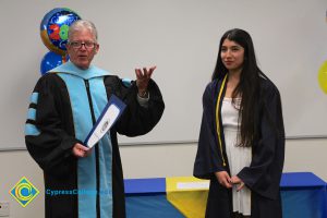President Bob Simpson, holding a certificate with a young lady in her graduation gown,