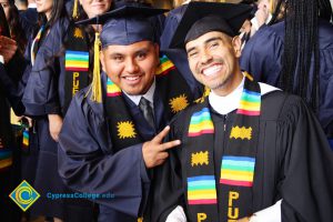 Two young men in graduation cap and gown smiling.
