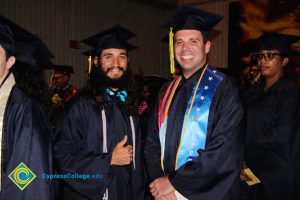 Two young men in graduation cap and gown smiling.
