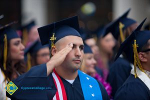 A graduate in cap and gown saluting the flag during the 48th Commencement.