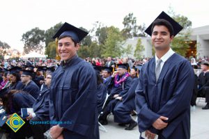 Two young men in graduation cap and gown smiling.