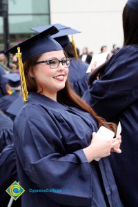 A young lady in graduation cap and gown smiling during the 48th Commencement.