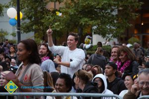 A young man in a white shirt holding up a pointing finger during commencement.