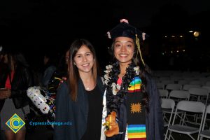A young woman in her cap and gown smiling with another young woman.