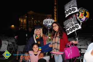 A young woman in her cap and gown with three children an a woman in a red sweater holding balloons.