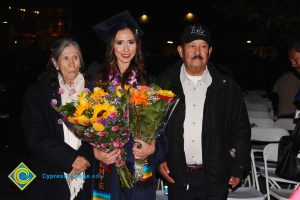 A young woman in cap and gown holding flowers with an older couple.