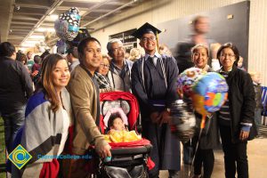 A young man in cap and gown smiling with his family by his side.