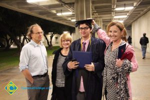 A young man in graduation cap and gown, with family and friends celebrating with him at the 48th Commencement.