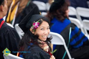A smiling young lady in her cap and gown with flowers in her hair during commencement.