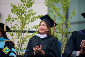 A woman in cap and gown smiling and applauding.